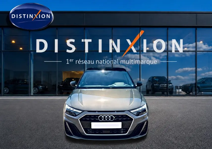 Audi A1 Sportback gris chronos vue de face, avec calandre noire et phares LED devant un showroom Distinxion.