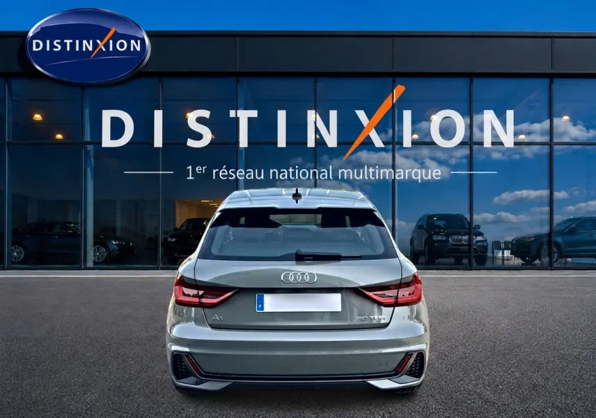 Vue arrière d'une Audi A1 Sportback gris chronos avec feux LED et becquet arrière, stationnée devant une vitrine Distinxion.