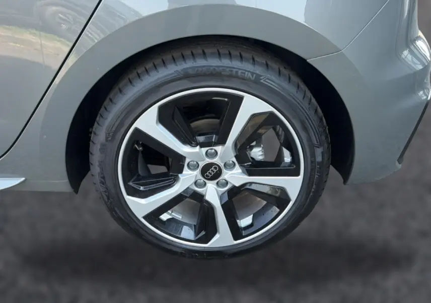Gros plan sur la jante alu bicolore côté arrière droit d’une Audi A1 Sportback gris chronos avec partie arrière du véhicule visible.