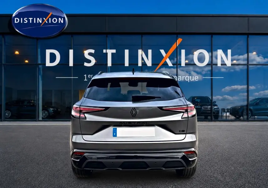 Vue arrière d'un Renault Austral gris schiste garé devant une vitrine avec logo Distinxion visible.