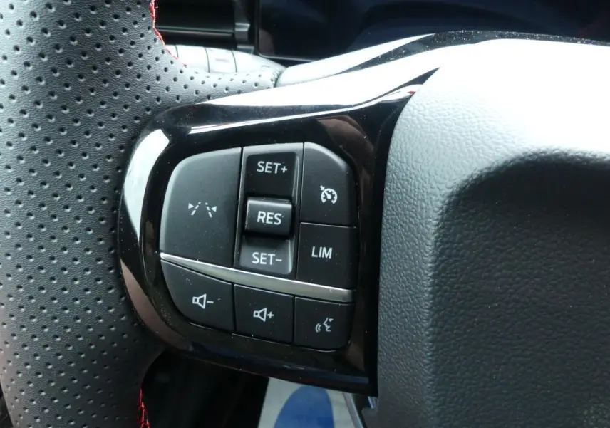 Gros plan sur les commandes de régulateur et volume au volant perforé avec surpiqûres rouges du Ford Puma gris métallisé 2025.