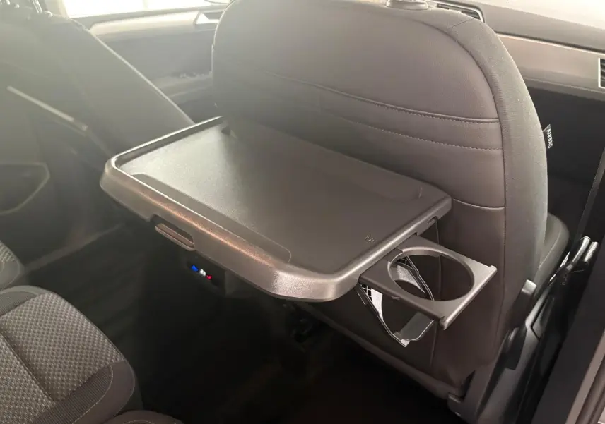 Tablette rabattable avec porte-gobelet sur le dossier du siège avant dans l'habitacle gris du Volkswagen Touran 2025.