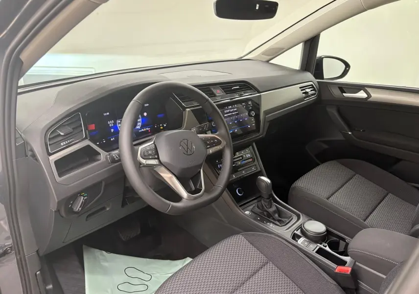 Intérieur du Volkswagen Touran gris dauphin 2025, vue côté conducteur montrant le tableau de bord et la console centrale moderne.