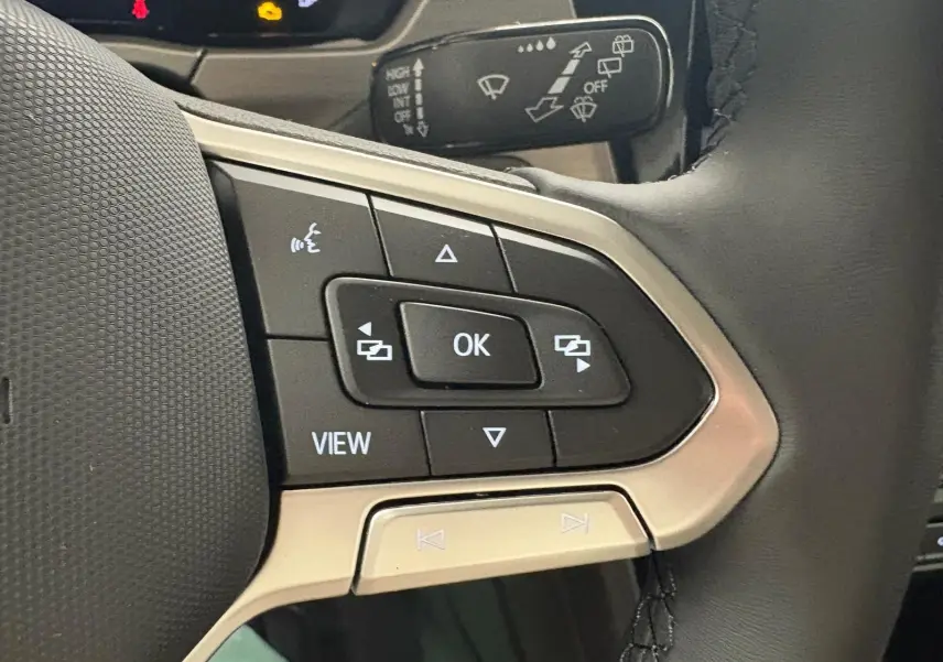 Gros plan sur les commandes multifonctions à gauche du volant cuir du Volkswagen Touran gris Dauphin 2025.