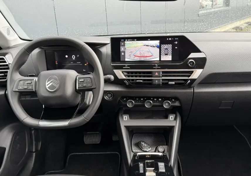 Vue intérieure avant du tableau de bord et volant de la Citroën C4 hybride 2025 avec écran tactile affichant la caméra de recul.