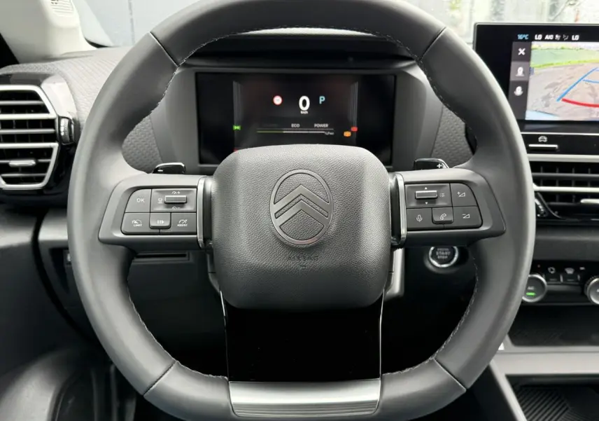 Vue centrée sur le volant cuir noir de la Citroën C4 2025 avec commandes intégrées et écran numérique en arrière-plan