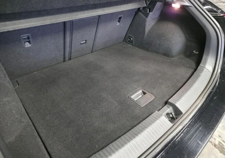 Vue intérieure du coffre spacieux et propre du Volkswagen T-Roc noir, avec éclairage latéral et revêtement en tissu gris foncé.