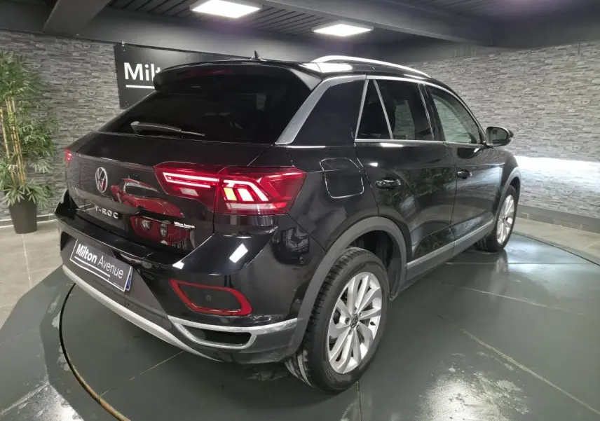 Volkswagen T-Roc noir vue 3/4 arrière droit en intérieur avec feux arrière LED allumés et jantes alliage.