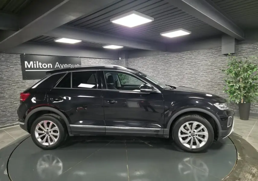 Volkswagen T-Roc noir en profil droit dans un showroom avec jantes alliage 17 pouces et vitres surteintées.