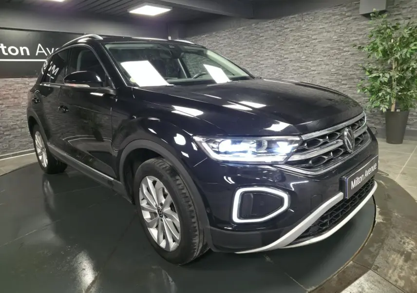 Volkswagen T-Roc noir métallisé vu en 3/4 avant droit avec phares LED allumés en showroom.
