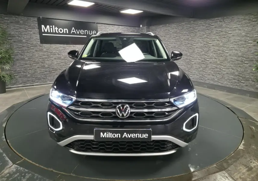 Volkswagen T-Roc noir vu de face, avec feux LED allumés et calandre chromée dans un showroom.