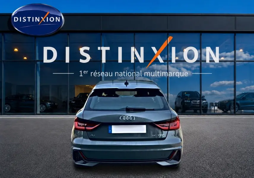 Vue arrière d'une Audi A1 Sportback gris chronos avec feux LED et becquet arrière, stationnée devant une vitrine Distinxion.