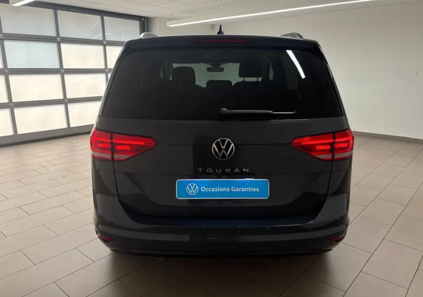 Vue arrière d'un Volkswagen Touran gris dauphin 2025 avec feux LED et logo VW bien visibles dans un garage.