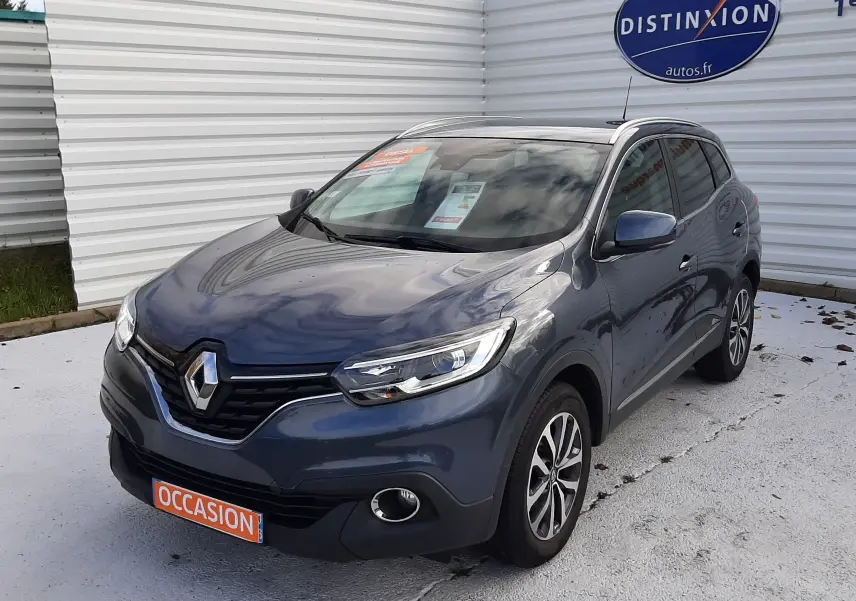 Renault Kadjar gris en 3/4 avant droit, avec phares LED et jantes alliage, stationné devant un mur blanc.