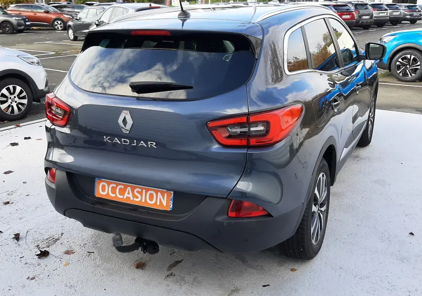 Vue 3/4 arrière droite d'un Renault Kadjar gris 2018 avec plaque "OCCASION" sur un parking extérieur.