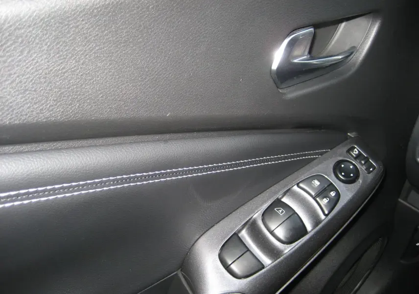 Gros plan sur la commande des vitres et rétroviseurs côté gauche du Nissan Juke 1.6 Hybrid 143 Tekna noir intérieur.