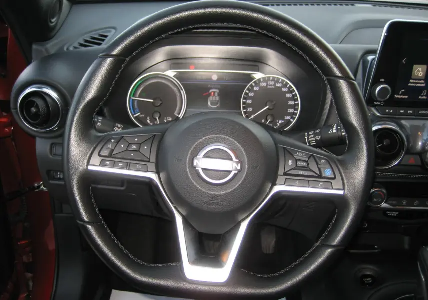 Vue rapprochée du volant en cuir noir du Nissan Juke rouge 2024, avec tableau de bord et écran tactile visibles.
