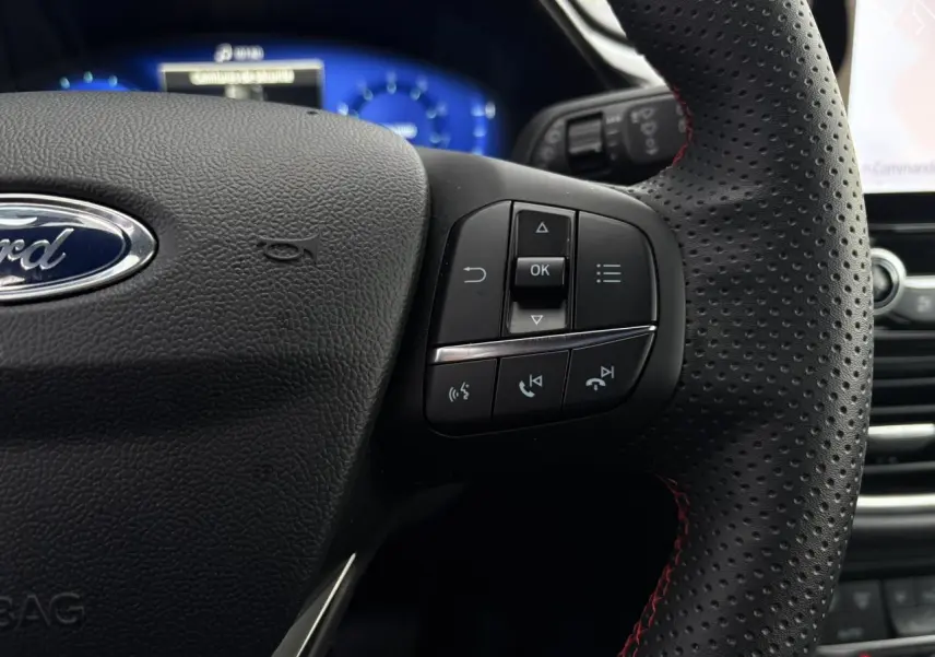 Gros plan sur le volant perforé ST-Line de la Ford Puma 2023 avec commandes intégrées et coutures rouges visibles.