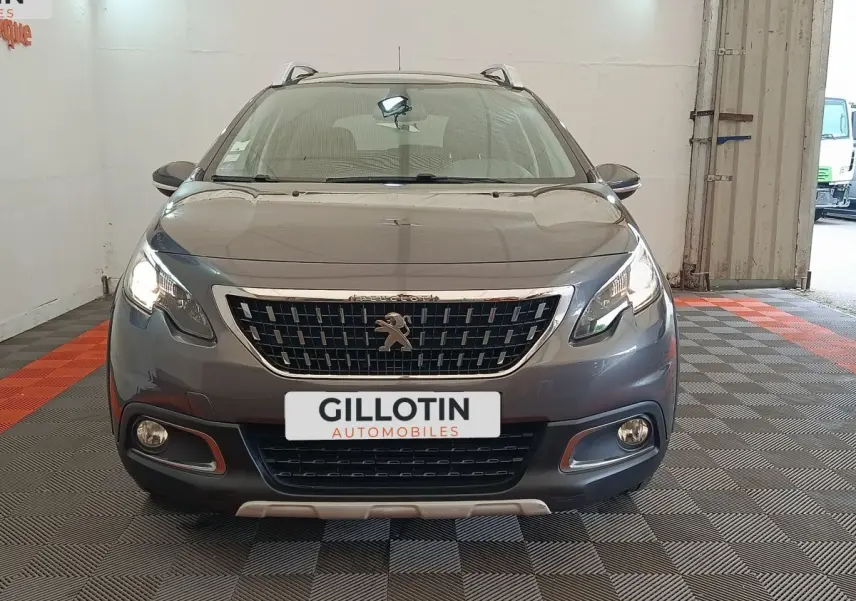 Vue de face d'un Peugeot 2008 gris foncé avec calandre chromée et feux allumés dans un garage.