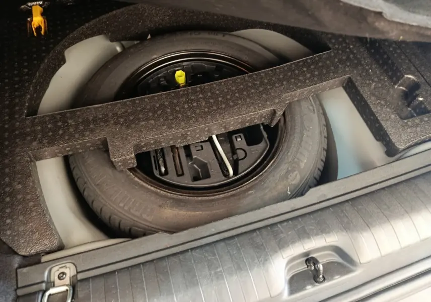 Vue rapprochée de la roue de secours dans le coffre d’un Peugeot 2008 gris foncé, avec outils de changement intégrés.