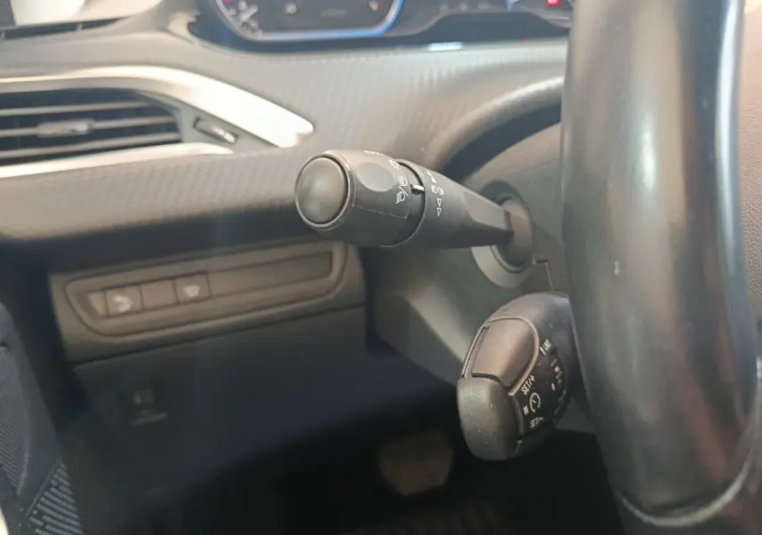 Gros plan sur la colonne de direction du Peugeot 2008 gris foncé, avec commandes de phares et régulateur de vitesse visibles.