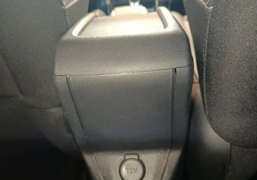 Vue intérieure arrière centrée sur la console centrale noire avec prise 12V entre les sièges avant du Peugeot 2008 gris foncé.