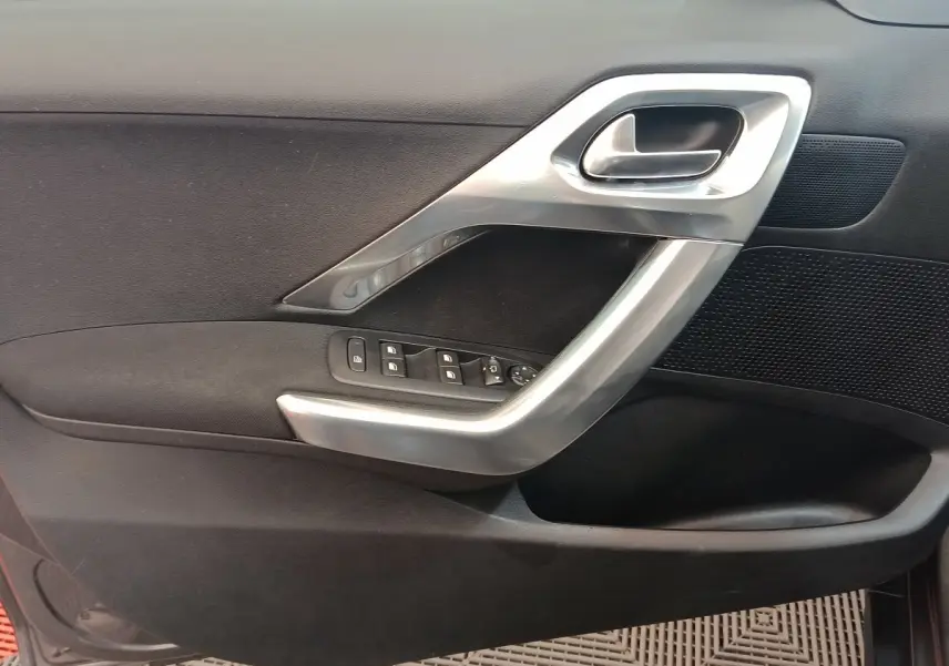 Détail de la porte intérieure côté gauche de Peugeot 2008 gris foncé avec poignée argentée et commandes des vitres.