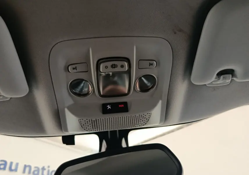 Vue intérieure en contre-plongée du plafonnier gris clair avec commandes d’éclairage et bouton SOS du Peugeot 2008 gris foncé.