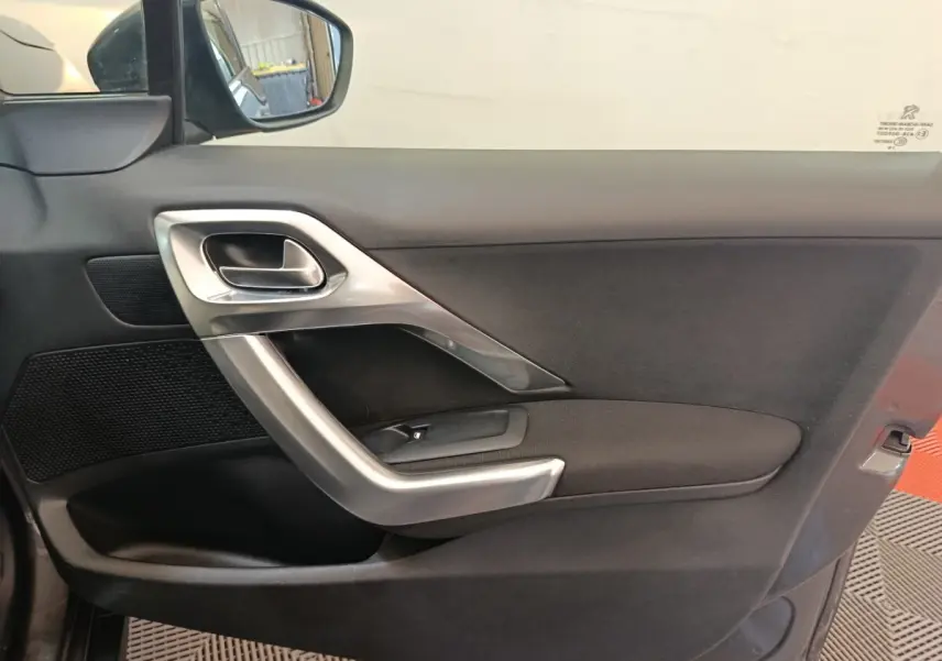 Vue intérieure côté gauche de la porte avant d'une Peugeot 2008 gris foncé avec poignée argentée et commande de vitre.