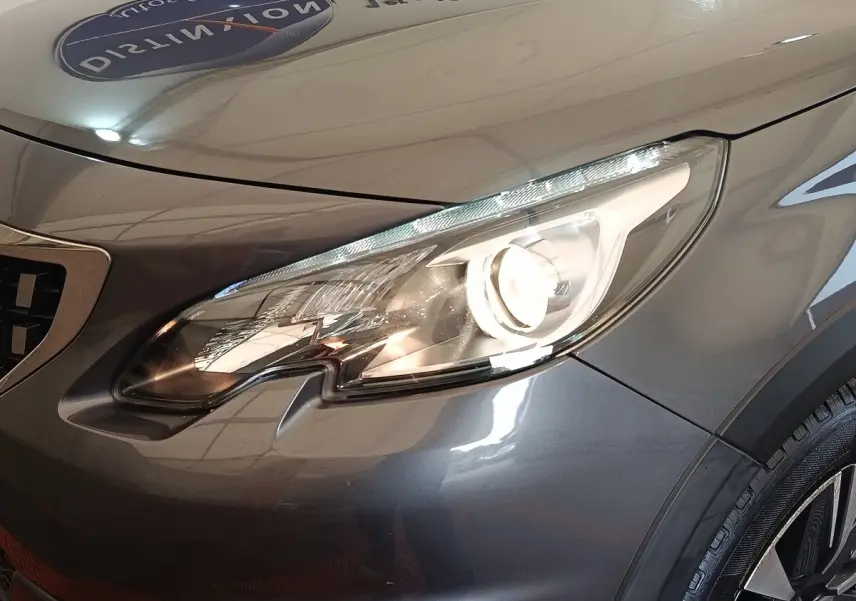Gros plan sur le phare avant droit d’un Peugeot 2008 gris foncé, mettant en valeur les lignes modernes et le capot lisse.