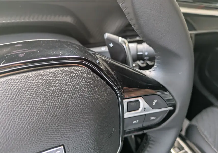 Gros plan sur la partie droite du volant cuir du Peugeot 2008 Hybrid 145, avec commandes intégrées et palettes au volant.