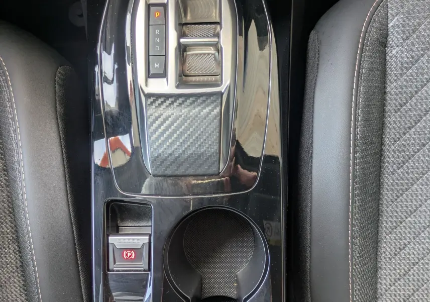 Vue plongeante sur la console centrale noire brillante du Peugeot 2008 Hybrid 145, avec levier de vitesses et sellerie tissu gris.