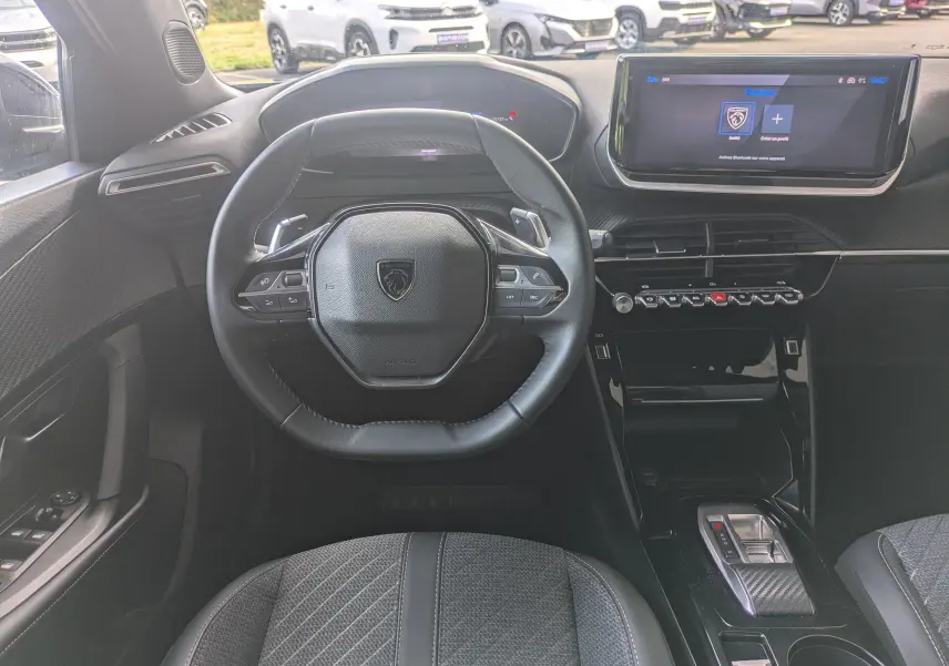 Vue intérieure centrée sur le volant compact et le tableau de bord numérique du Peugeot 2008 Hybrid 145, sellerie tissu grise.