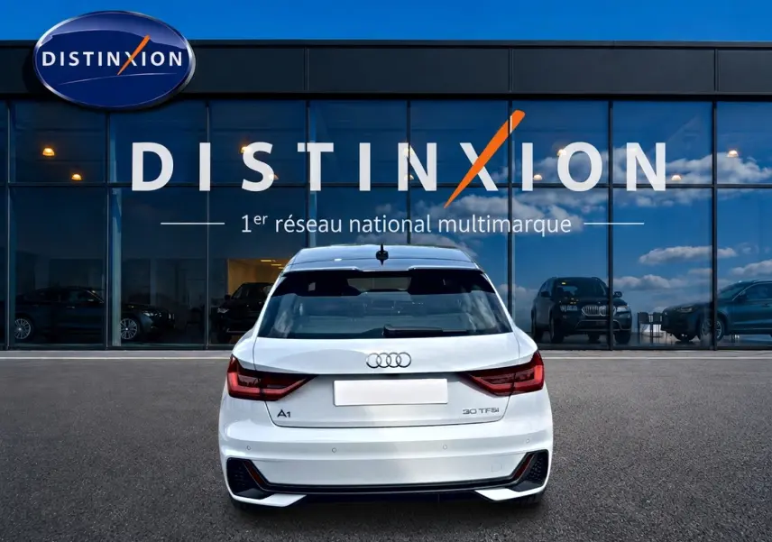 Vue arrière d'une Audi A1 Sportback blanc et noir, avec feux LED et becquet arrière, stationnée devant une vitrine Distinxion.