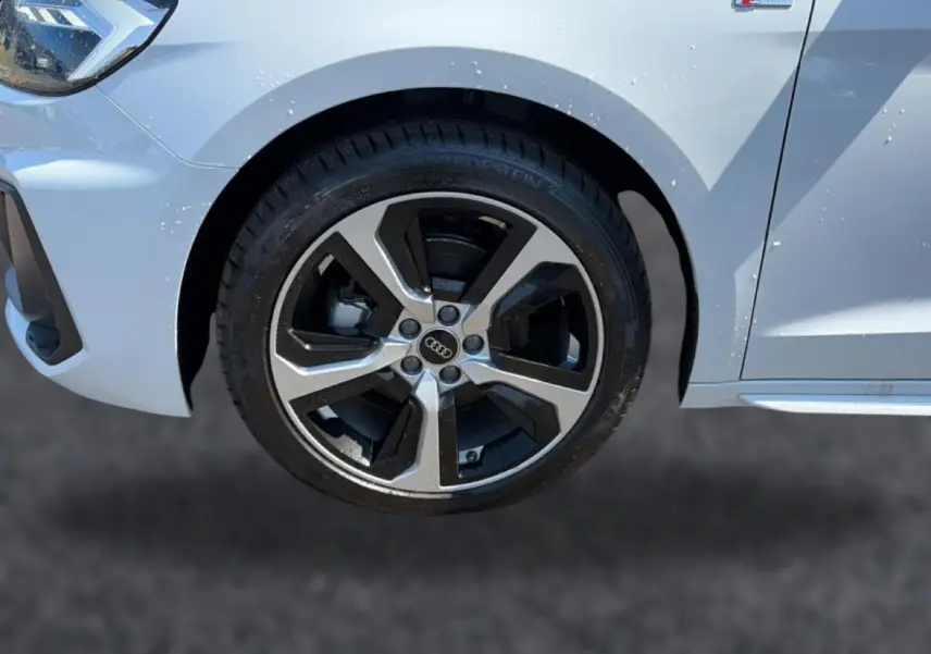 Gros plan sur la roue avant gauche et l’aile blanche de l’Audi A1 Sportback 30 TFSI S line avec jante alu bicolore.