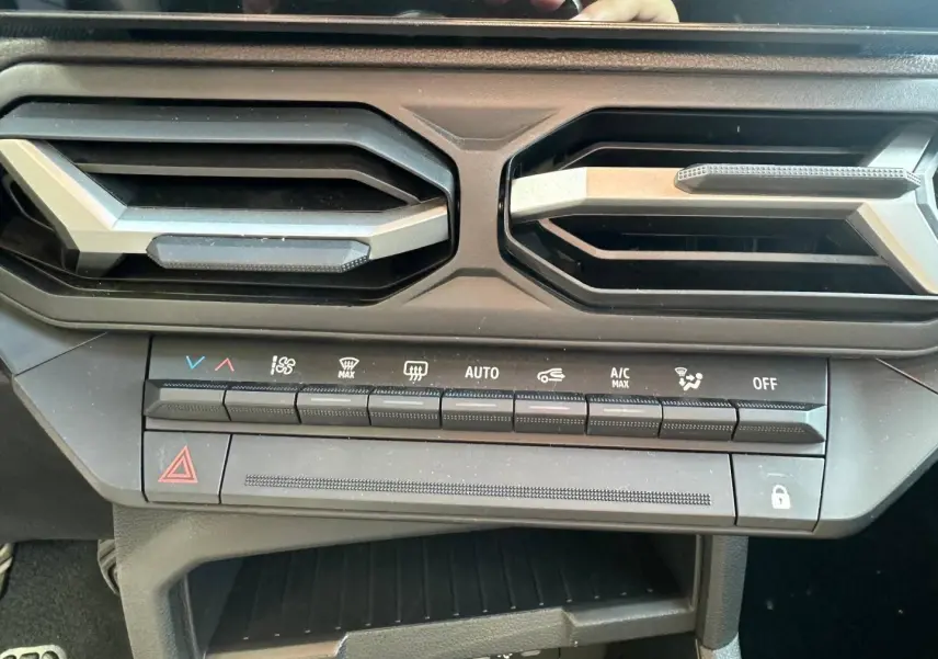 Vue rapprochée de la console centrale du Dacia Duster 2025, boutons de climatisation et aérateurs noirs.