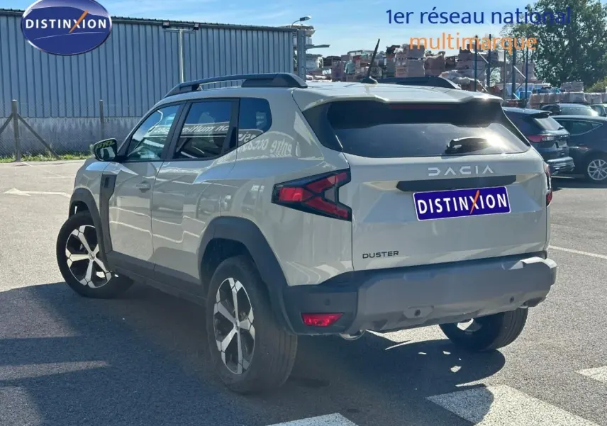 Vue 3/4 arrière droite du Dacia Duster 2025 couleur Sandstone avec barres de toit et jantes alliage.