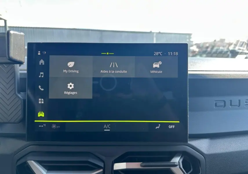 Vue rapprochée de l’écran tactile central du Dacia Duster 2025, affichant les aides à la conduite, avec tableau de bord noir.