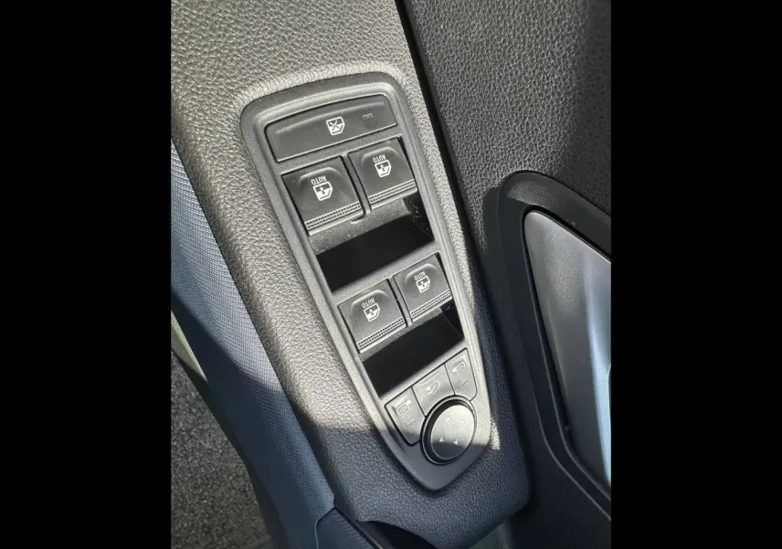Gros plan sur les commandes des vitres électriques et rétroviseurs côté conducteur du Dacia Duster 2025 couleur Sandstone.