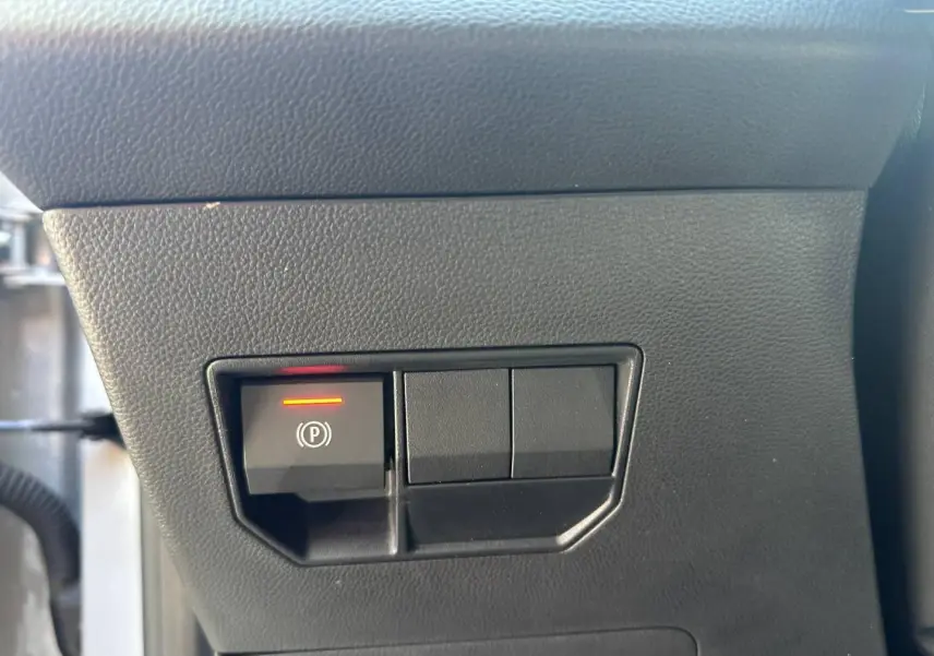 Bouton de frein de stationnement électronique allumé sur tableau de bord noir du Dacia Duster 2025.