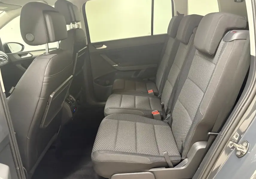 Vue latérale droite de l'habitacle arrière du Volkswagen Touran gris Dauphin 2025, montrant les trois sièges en tissu gris avec appuie-têtes.