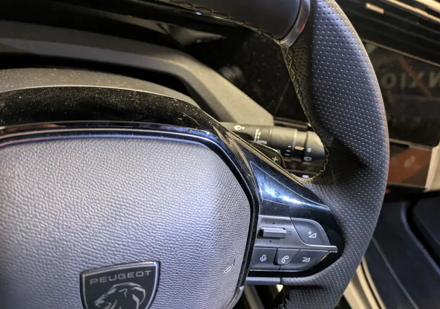 Gros plan sur le volant cuir perforé et les commandes multifonctions du Peugeot 308 SW Hybrid gris, côté conducteur.