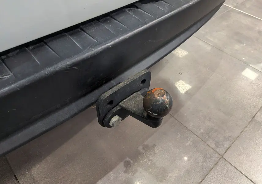 Gros plan sur l'attelage arrière noir d'un Renault Kangoo Express blanc minéral, vue du pare-chocs et boule d'attelage usée.