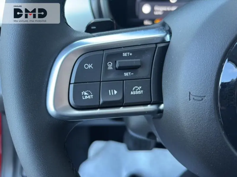 Gros plan sur les commandes multifonctions du volant côté gauche d'une FIAT 600 rouge, version hybride 2026.