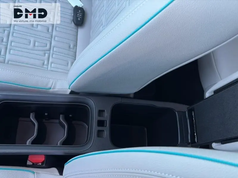 Vue plongeante sur l'accoudoir central ivoire avec surpiqûres bleues et porte-gobelets du Fiat 600 hybride rouge 2026.