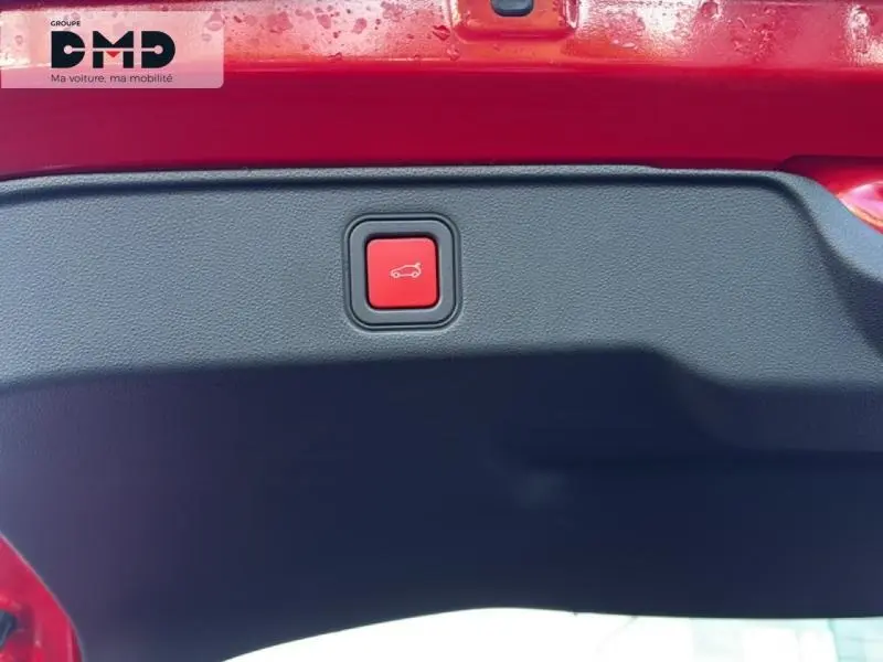 Bouton rouge d'ouverture électrique du coffre sur la partie intérieure du hayon d'une FIAT 600 rouge vue en gros plan.