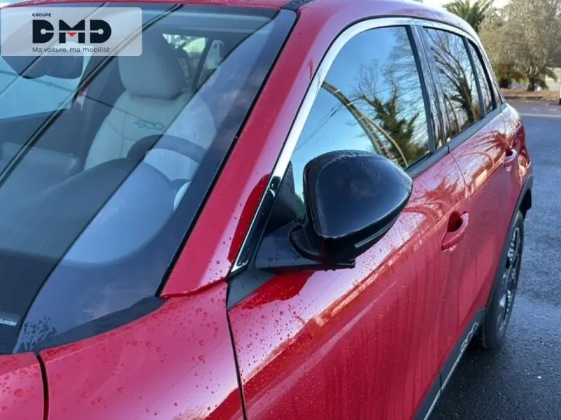 Vue rapprochée côté gauche avant d'une FIAT 600 rouge avec rétroviseur noir et intérieur clair visible.
