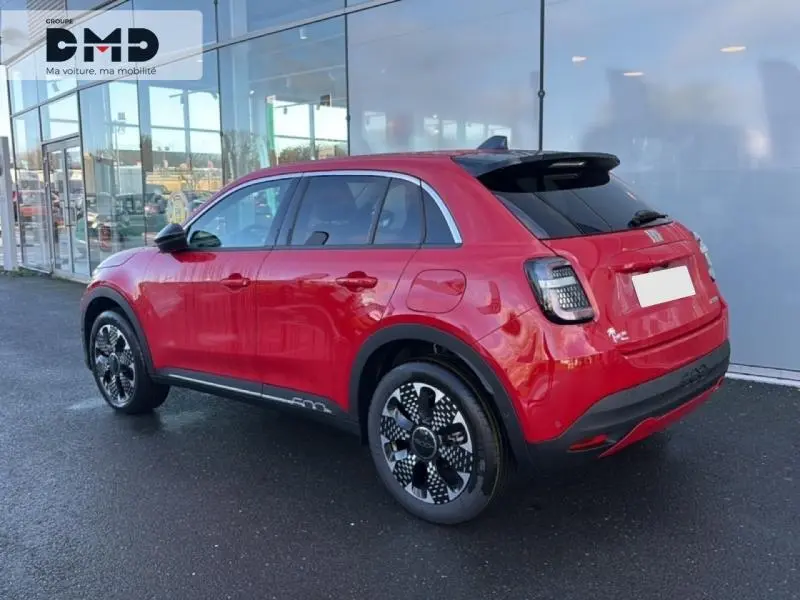 Vue 3/4 arrière droite d'une FIAT 600 rouge avec jantes noires et toit noir, stationnée devant une vitrine.
