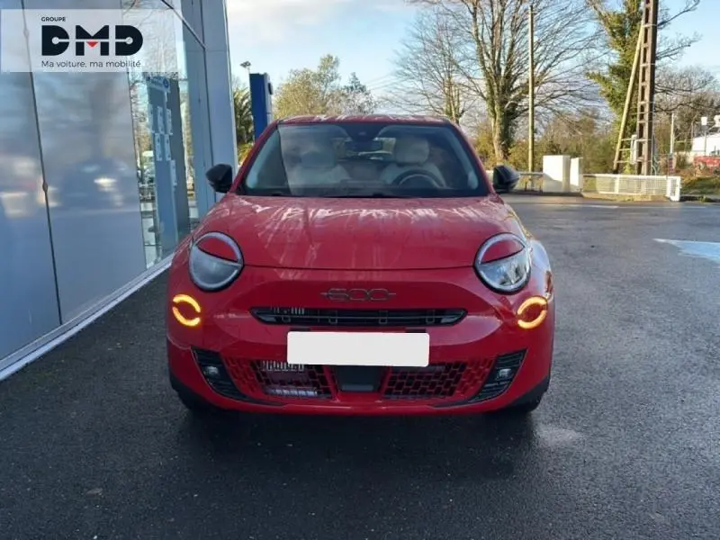 Vue frontale d'une FIAT 600 rouge avec feux de jour circulaires allumés, stationnée devant un bâtiment vitré.