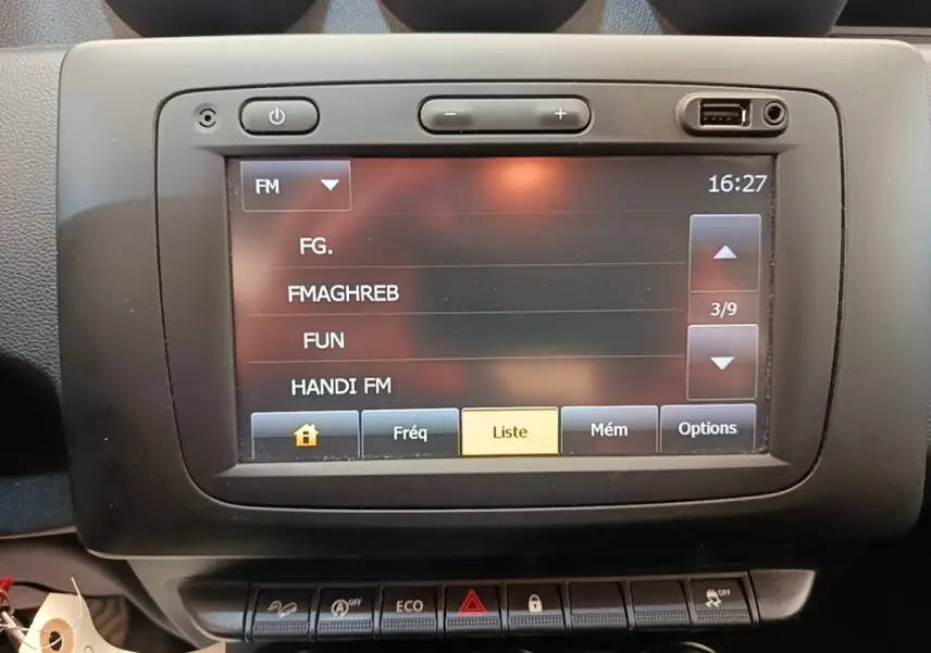 Écran tactile central du tableau de bord du Dacia Duster blanc, affichant les stations radio FM.
